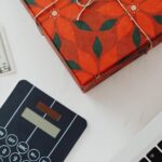 A beautifully wrapped gift box, cash, calculator, and laptop on a white table, symbolizing holiday expenses.