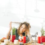 A woman with curly hair sits at a decorated dining table with candles and potted plants.