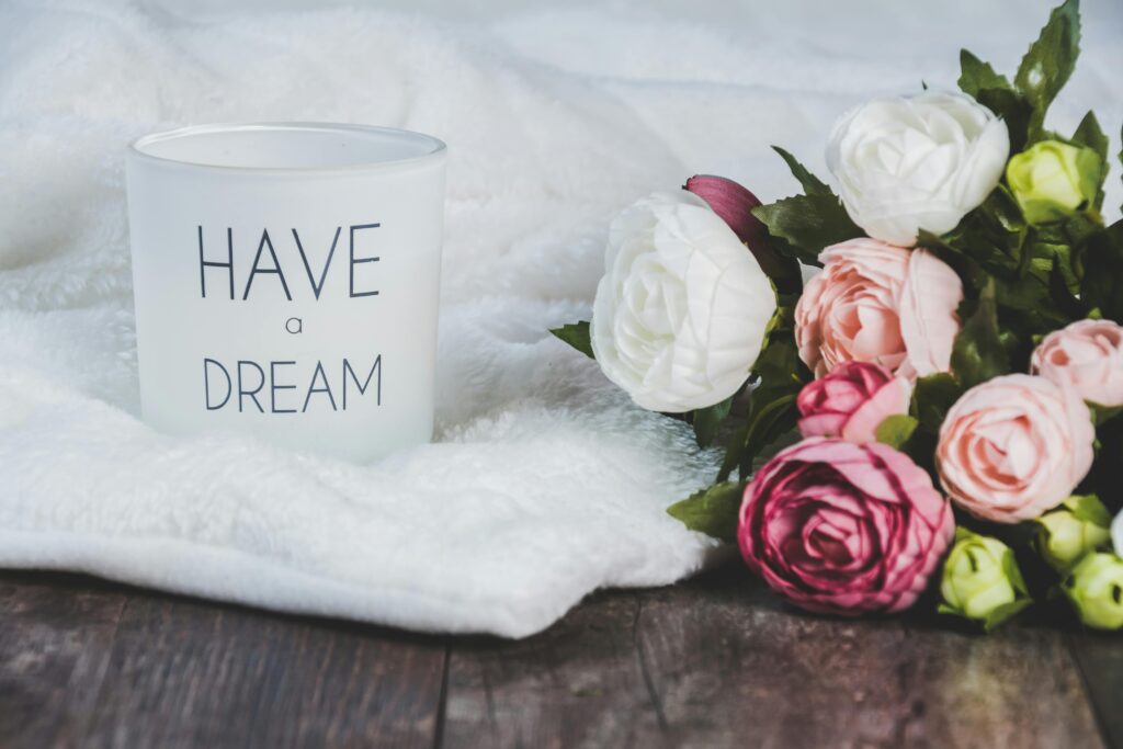 Soft focus image of a candle with 'Have a Dream' text beside a bouquet of roses on a blanket.