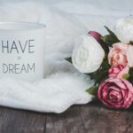 Soft focus image of a candle with 'Have a Dream' text beside a bouquet of roses on a blanket.