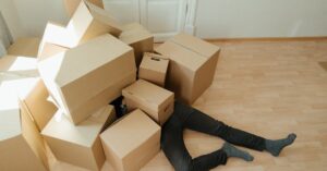 A person overwhelmed by cardboard boxes during a home move, symbolizing stress and relocation.